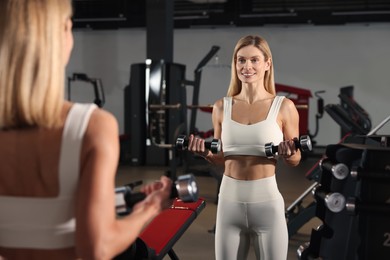 Photo of Woman training with dumbbells near mirror in gym