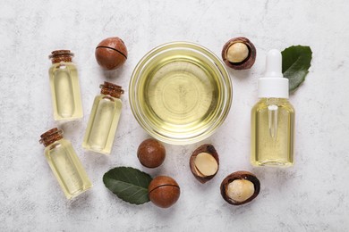 Delicious organic Macadamia nuts, natural oil and green leaves on white textured table, flat lay