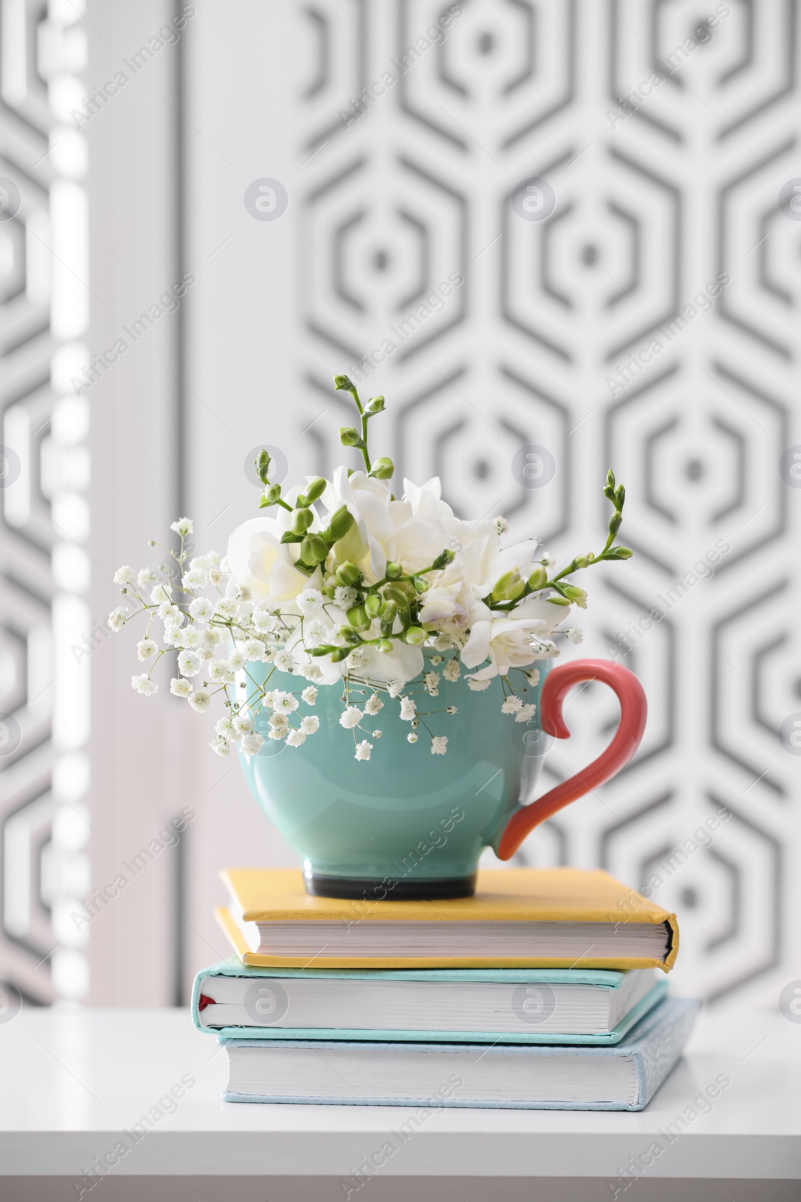 Photo of Beautiful bright flowers in cup and books on white table indoors