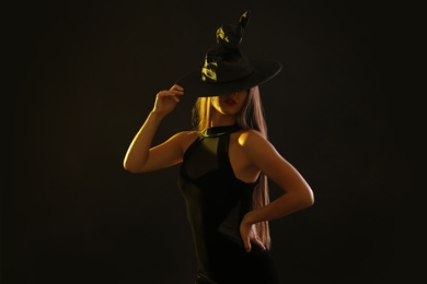 Photo of Young woman wearing witch costume on black background. Halloween party