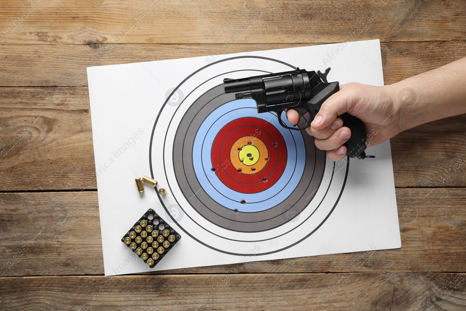 Photo of Man with handgun, shooting target and bullets on wooden table, top view