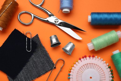 Flat lay composition with thimbles and different sewing tools on orange background