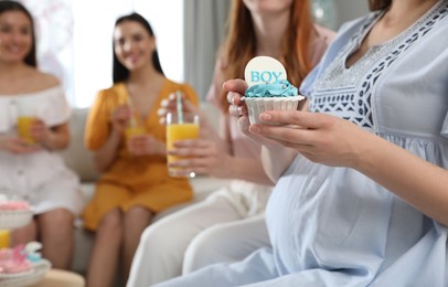 Photo of Pregnant woman with cupcake at home during baby shower party, closeup