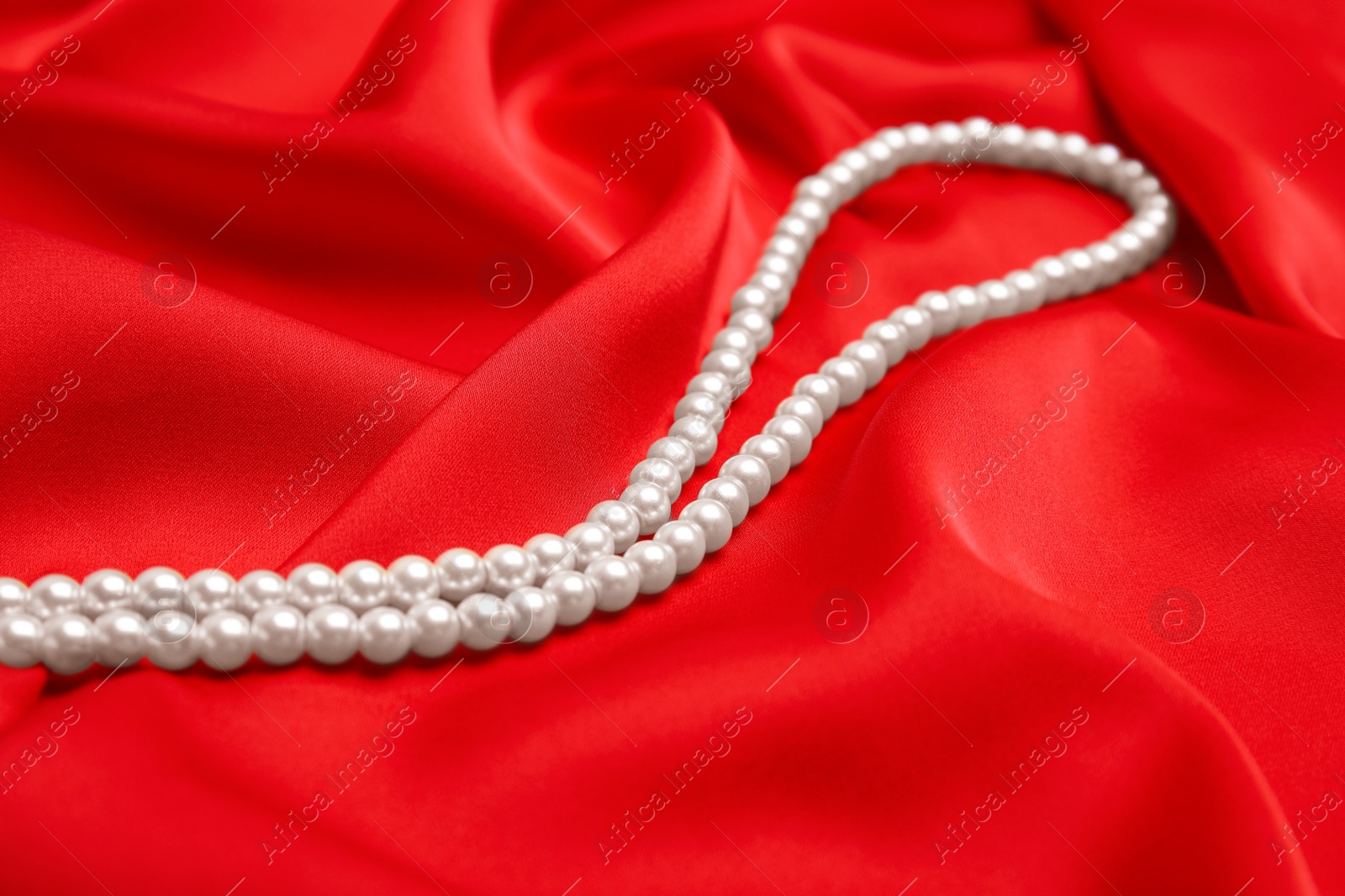 Photo of Beautiful white pearls on delicate red silk