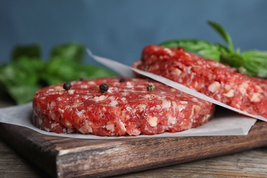 Photo of Raw meat cutlets for burger on wooden table against blue background, closeup