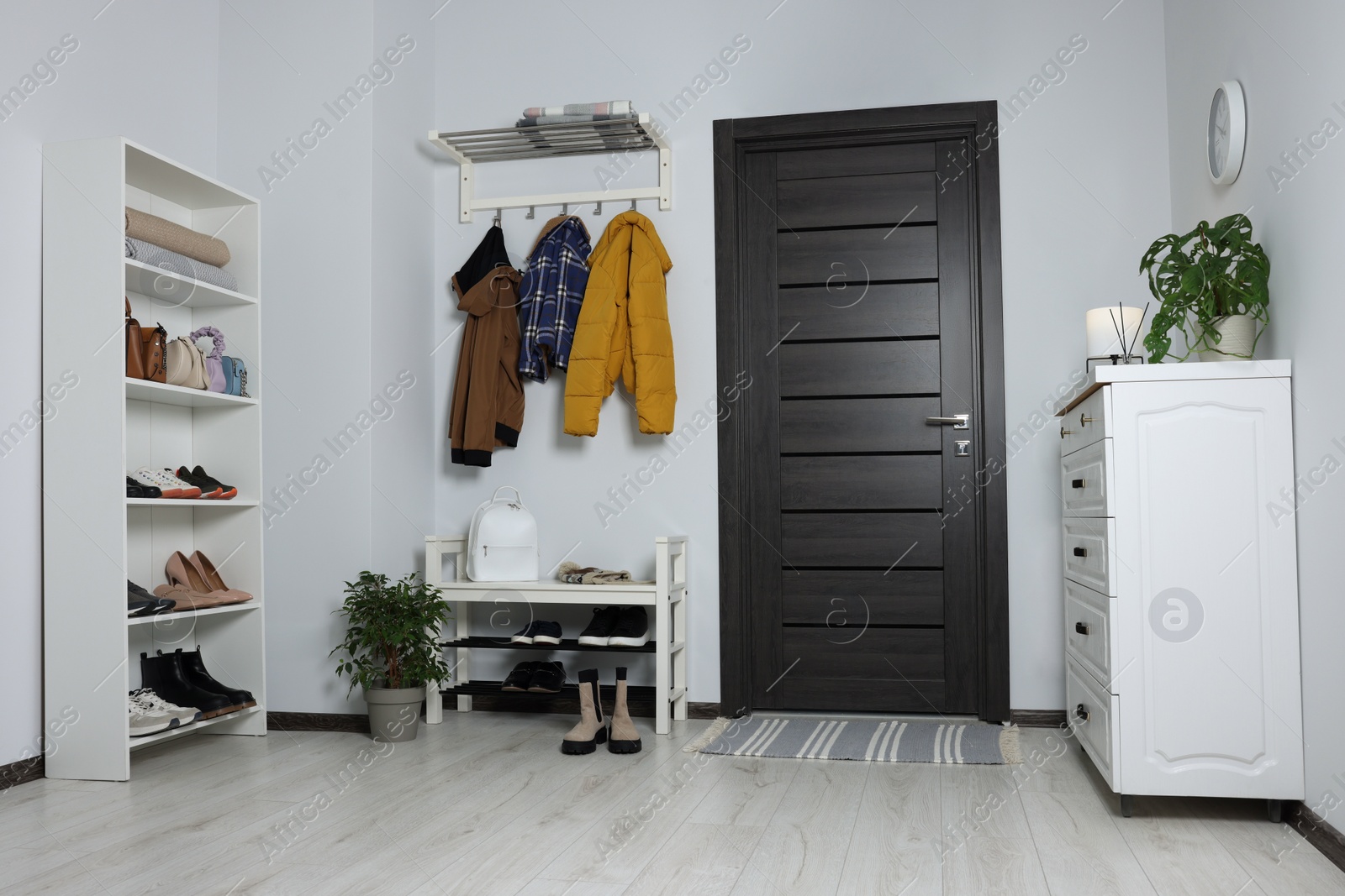 Photo of Beautiful hallway interior with coat rack, chest of drawers and shoe storage bench near wooden door