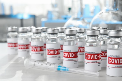Photo of Glass vials with COVID-19 vaccine and syringe on white wooden table