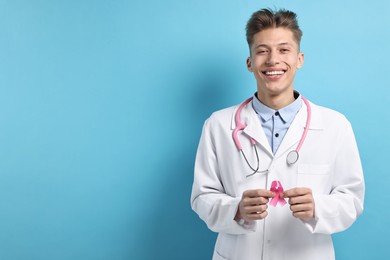 Photo of Mammologist with pink ribbon on light blue background, space for text. Breast cancer awareness