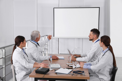 Photo of Team of doctors using video projector during conference indoors