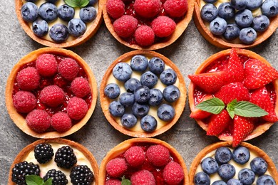 Photo of Tartlets with different fresh berries on light grey table, flat lay. Delicious dessert