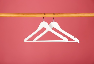 Empty clothes hangers on wooden rail against color background