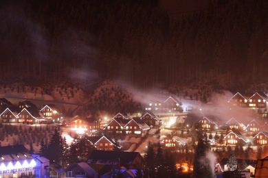 Night landscape with mountain village near forest in winter