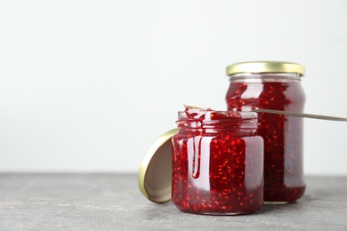 Jars of raspberry jam on grey table. Space for text