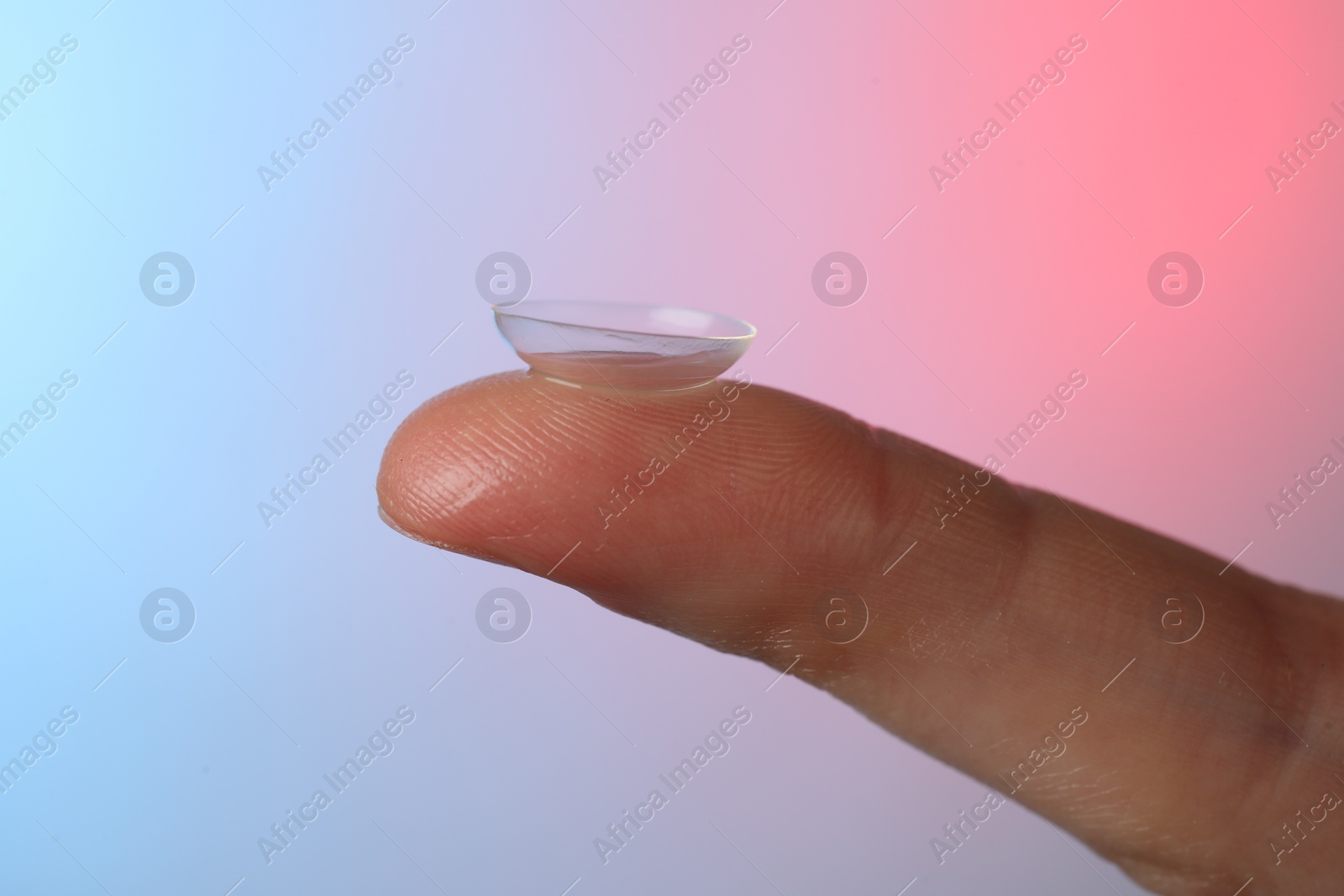 Photo of Woman holding contact lens on color background, closeup