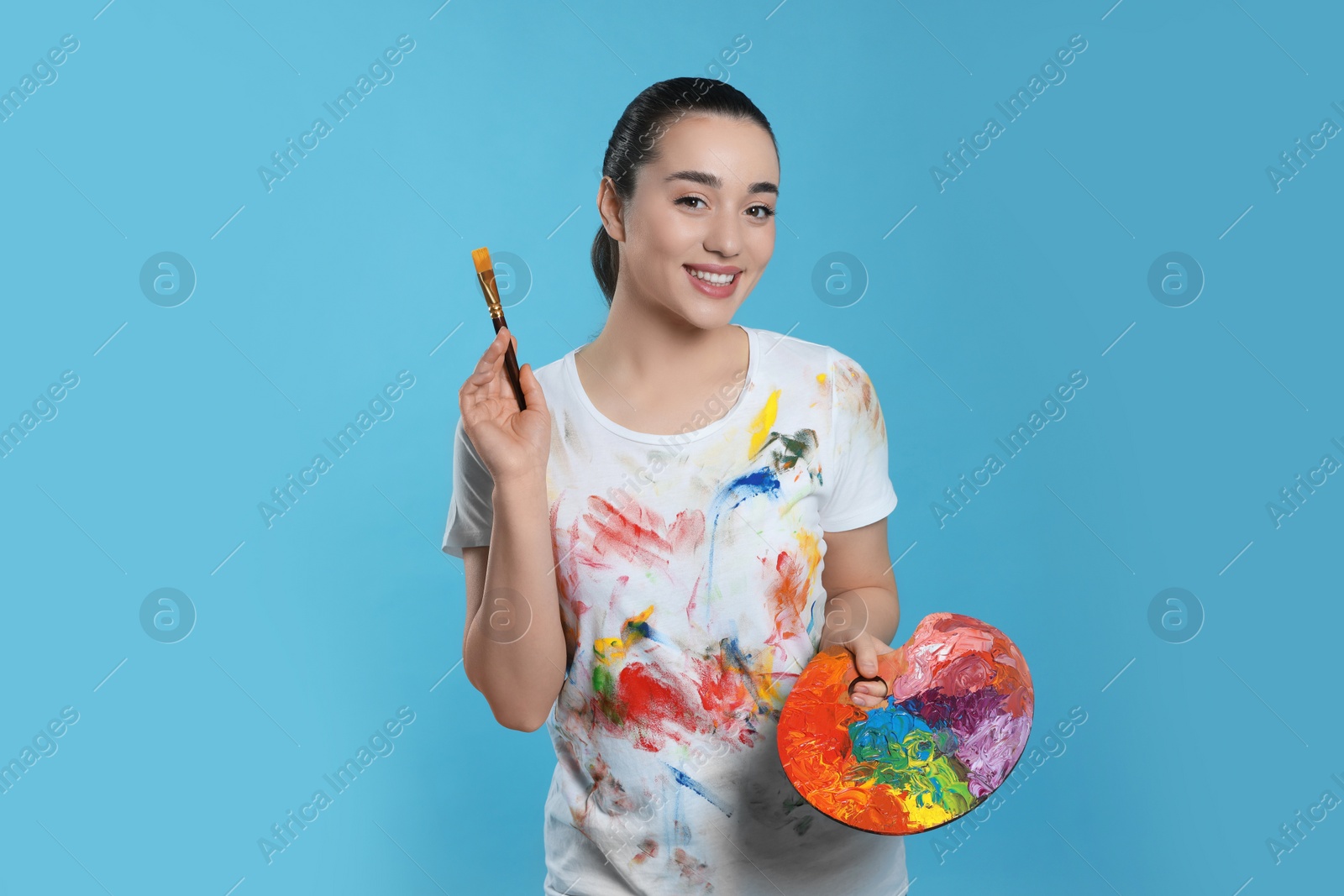 Photo of Woman with painting tools on light blue background. Young artist