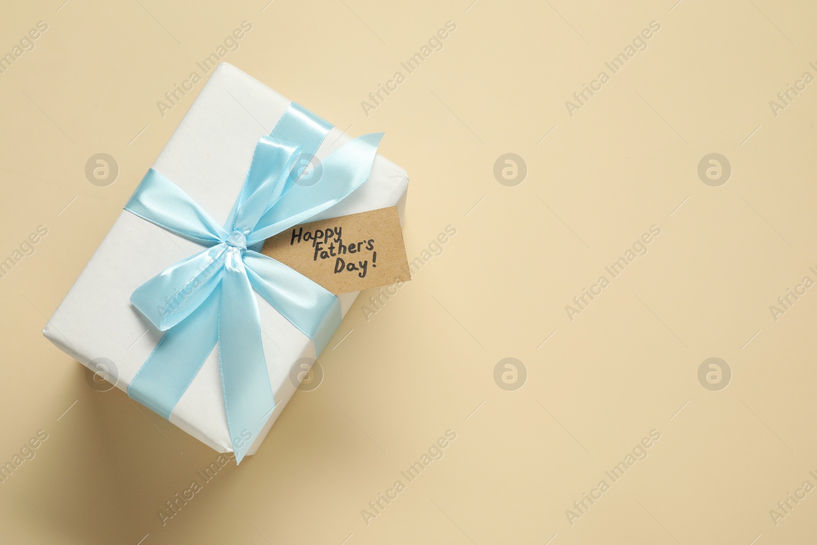 Photo of Card with phrase Happy Father's Day and gift box on beige background, top view. Space for text