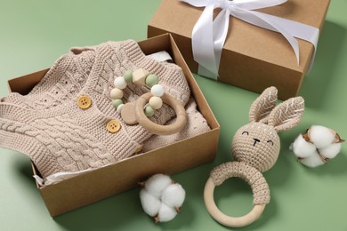 Photo of Different baby accessories, knitted clothes and cotton flowers on green background