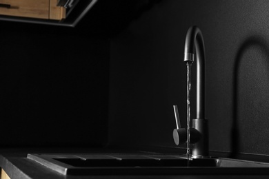 Photo of Closeup view of water flowing from faucet indoors. Space for text