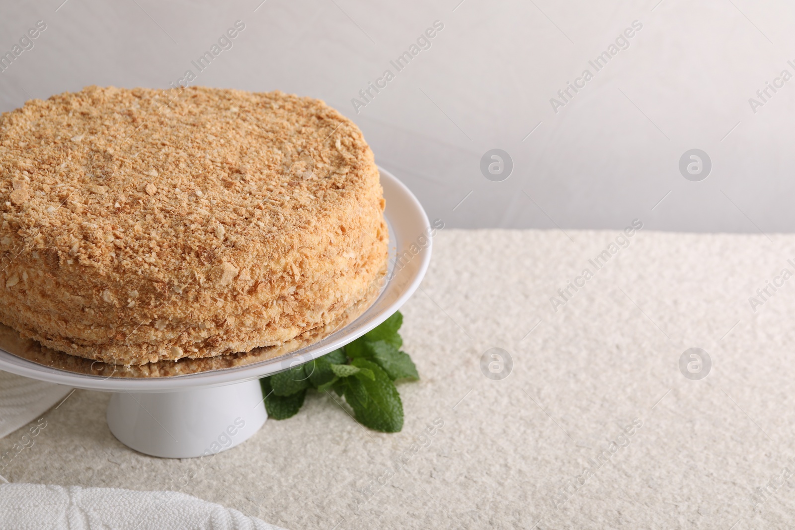 Photo of Delicious Napoleon cake and mint on beige table, closeup. Space for text