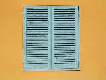 Photo of Window with closed wooden shutters on orange wall