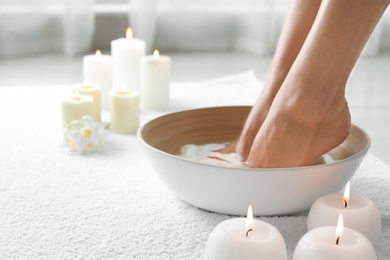 Photo of Woman soaking her feet in dish indoors, closeup with space for text. Spa treatment