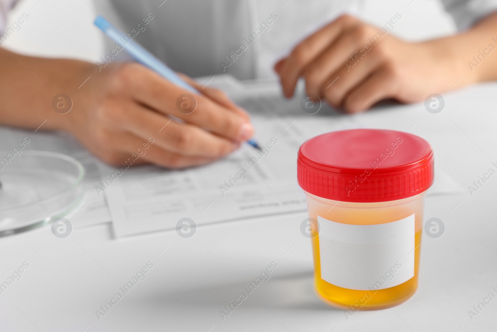 Photo of Closeup view of nurse writing urine analysis results at table, focus on container with sample