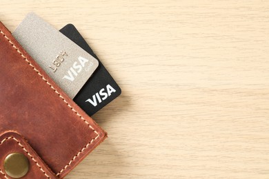 Photo of MYKOLAIV, UKRAINE - FEBRUARY 23, 2022: Bank cards of Visa payment system in leather wallet on wooden table, top view. Space for text