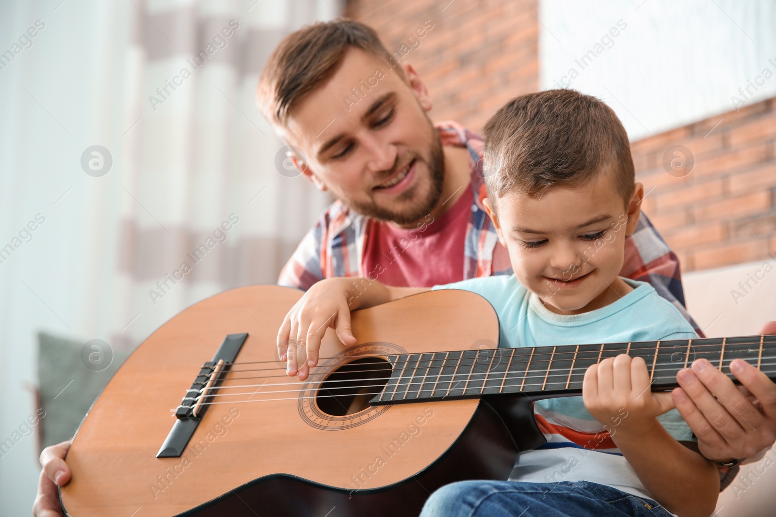 Photo of Father teaching his little son to play guitar at home