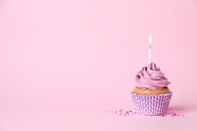 Delicious birthday cupcake with burning candle and sprinkles on pink background, space for text