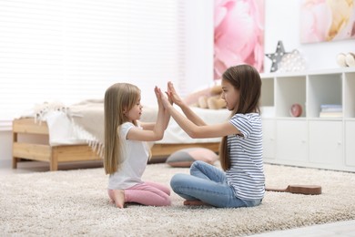 Photo of Cute little sisters playing clapping game with hands at home