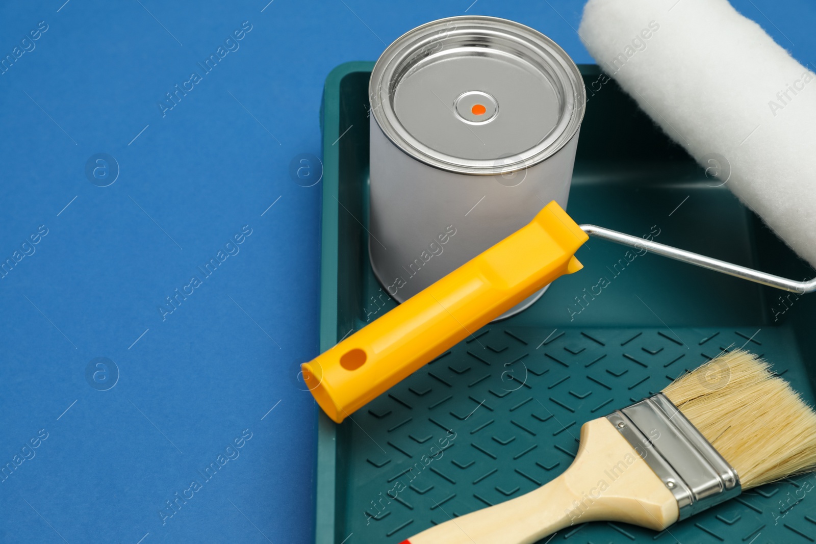 Photo of Can of orange paint, brush, roller and container on blue background. Space for text