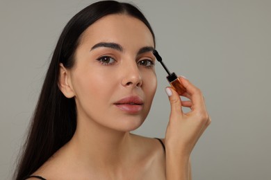 Beautiful young woman applying mascara on grey background