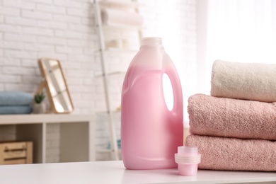 Bottle of detergent and clean towels on table indoors, space for text. Laundry day