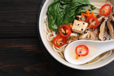 Photo of Bowl of vegetarian ramen and spoon on dark wooden table, top view. Space for text