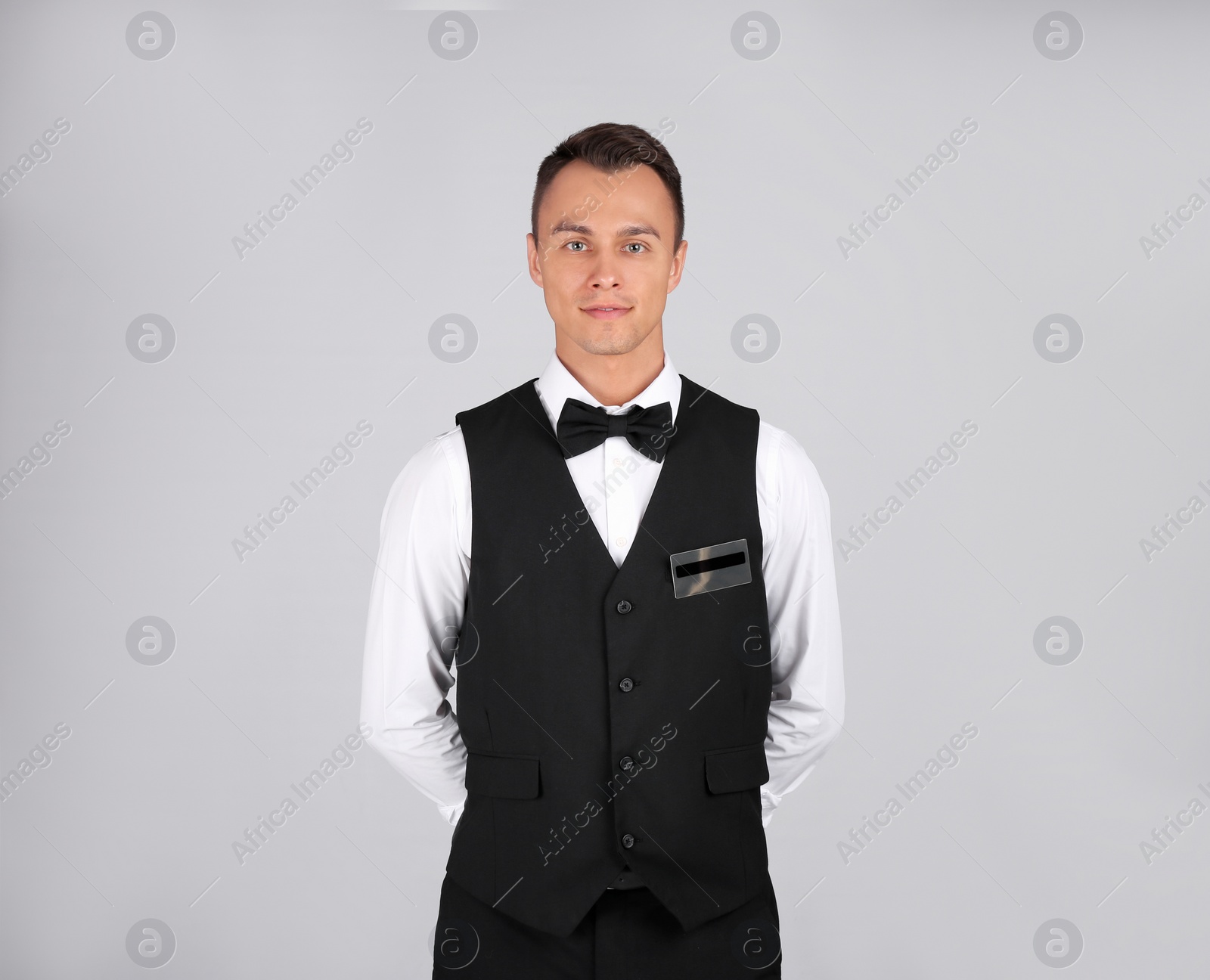 Photo of Portrait of young waiter in uniform on grey background