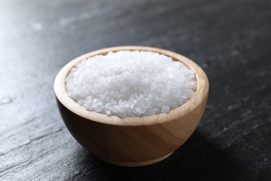 Photo of Organic white salt in bowl on black table, closeup