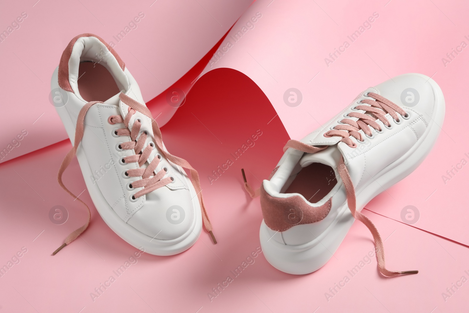 Photo of Pair of stylish shoes with laces on pink paper background