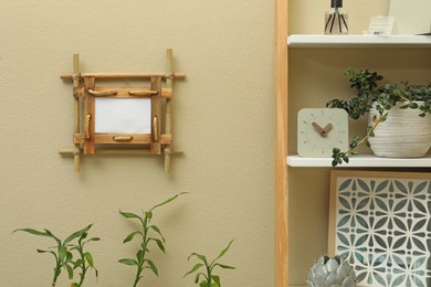 Photo of Decor elements on shelving unit near beige wall with bamboo frame indoors