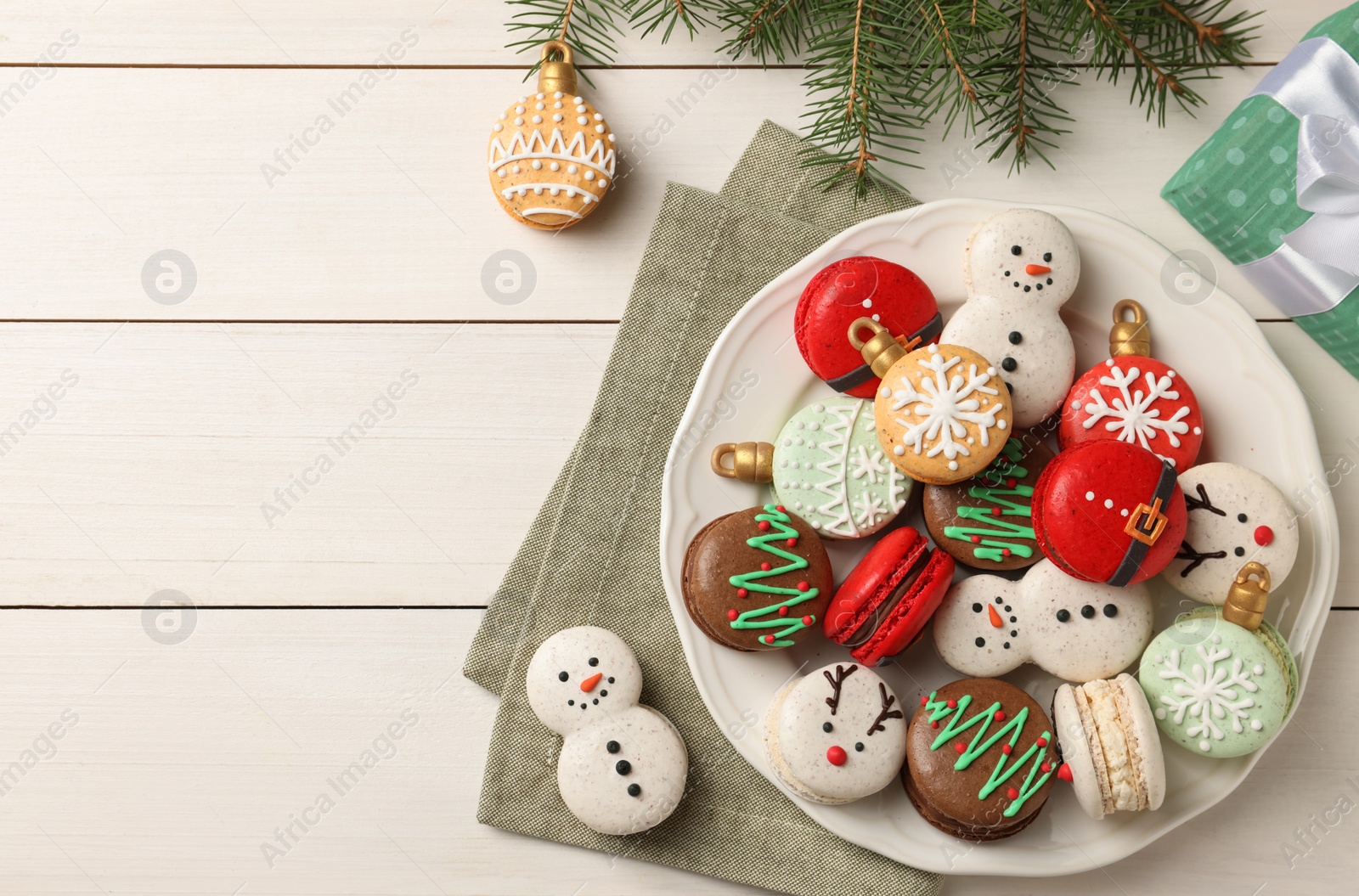 Photo of Beautifully decorated Christmas macarons and fir branches on white wooden table, flat lay. Space for text