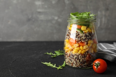 Jar with healthy quinoa salad and vegetables on table. Space for text