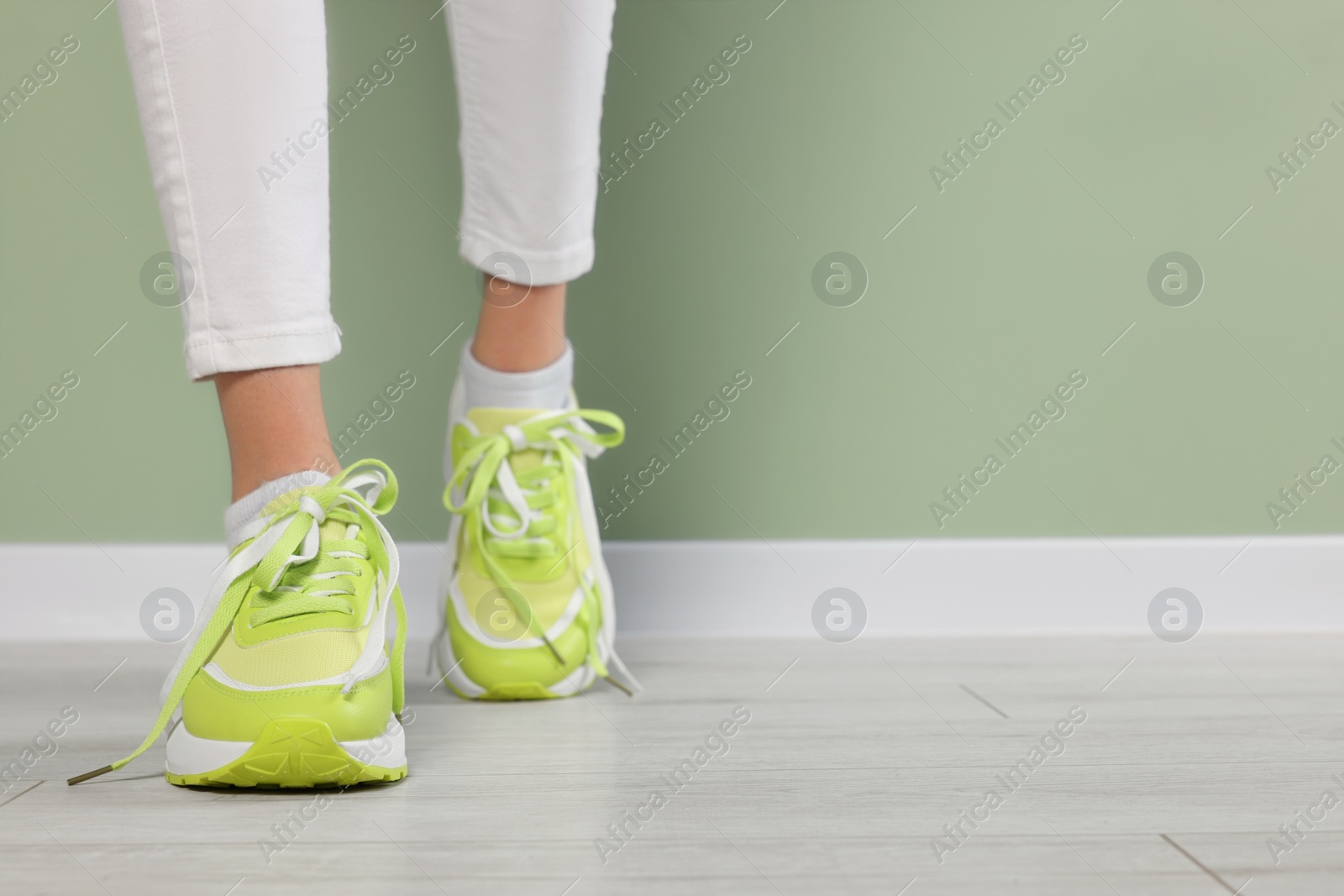 Photo of Woman wearing new stylish sneakers near light green wall, closeup. Space for text