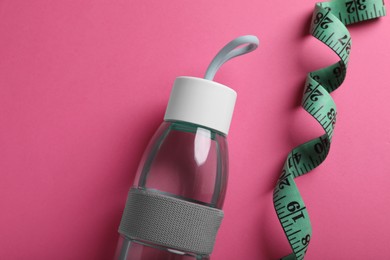 Measuring tape and bottle with water on pink background, flat lay. Weight control concept