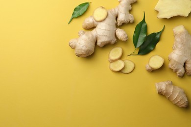 Photo of Fresh ginger with green leaves on pale light yellow background, flat lay. Space for text