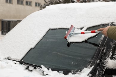Woman cleaning car windshield from snow with squeegee outdoors, closeup