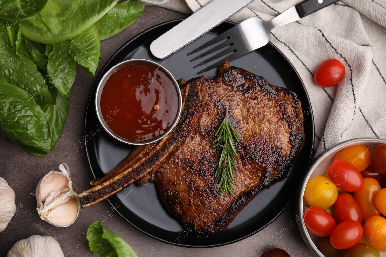 Photo of Tasty grilled meat, rosemary and marinade served on brown textured table, flat lay