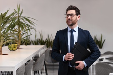 Photo of Happy real estate agent with leather portfolio indoors. Space for text