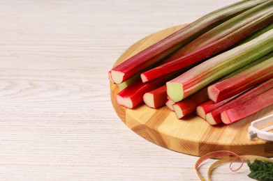 Photo of Cut fresh rhubarb stalks on white wooden table, space for text