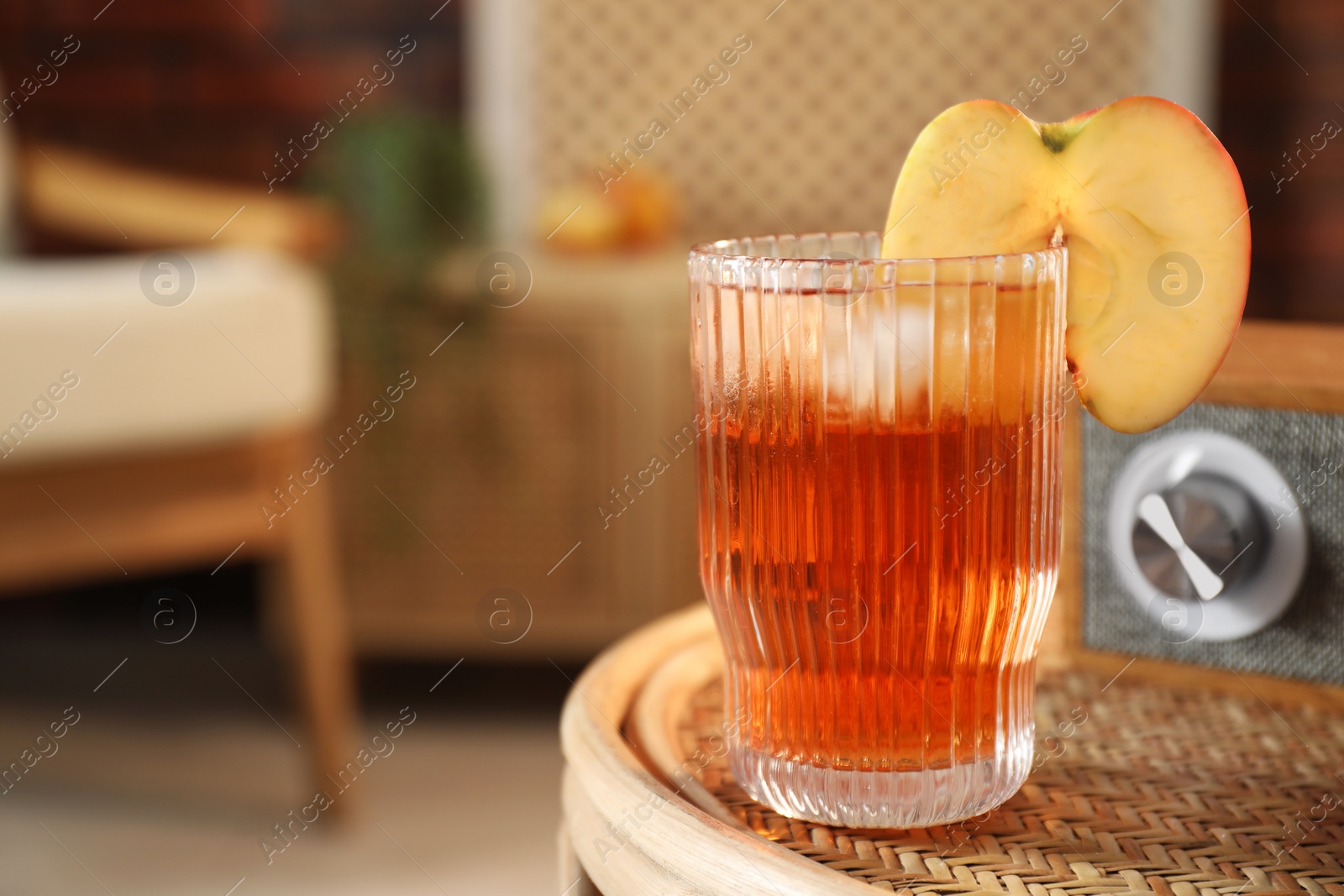 Photo of Relax at home. Glass of tasty cider on wicker table in room, closeup. Space for text