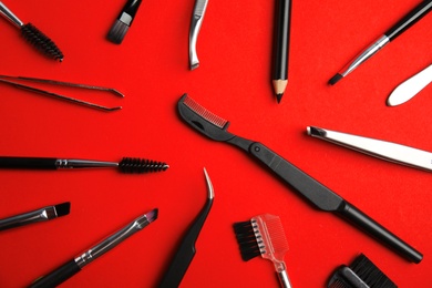 Set of professional eyebrow tools on red background, flat lay