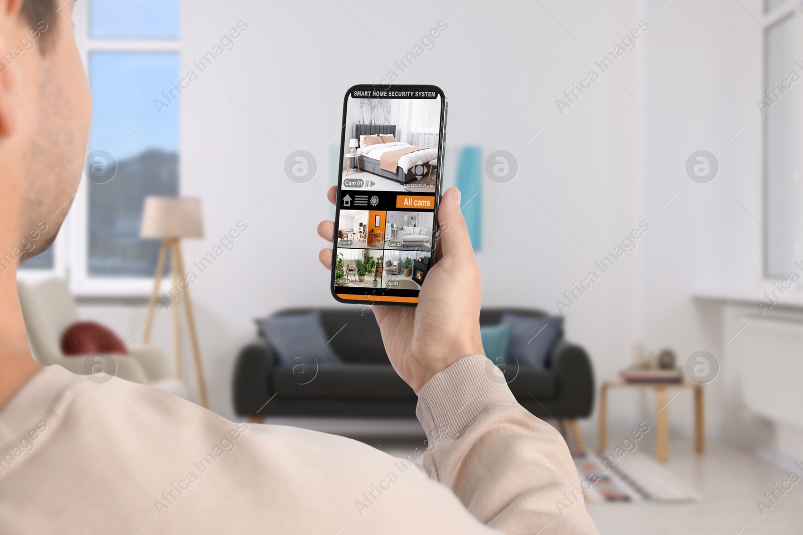 Image of Man using smart home security system on mobile phone indoors, closeup. Device showing different rooms through cameras